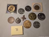Photo of entire collection of 11 assorted tokens, medals, and badges laid out on a flat surface with yellow paper marked '71'.