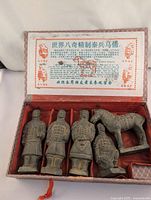 Five terra cotta figurines including four soldiers and one horse in original red fabric-lined box with an informational card inside the lid.