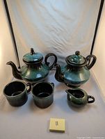 Full set showing two teapots, two mugs, and one creamer with green and black glaze finish.