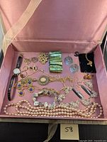 Open jewelry box showing assortment of vintage and modern costume jewelry including bracelets, necklaces, rings, earrings, and watches