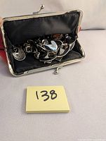 Jewelry inside small black fabric purse with silver frame closure. Contains mixed silver-tone jewelry items including chains and pendants.