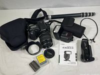 Complete view of all camera gear included in the lot, showing DSLR body, lens, Speedlite flash with case, monopod, VG10 vertical grip, shutter release cable, batteries, and soft case.