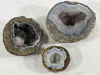 Three geode specimens arranged with rough exterior and crystal interiors visible