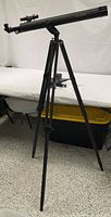 Full view of assembled black refractor telescope mounted on wooden tripod.