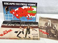 Front view of unopened Escape from New York board game box, game board displayed behind with colorful city map graphic. Clint Eastwood movie poster placed to the right side.