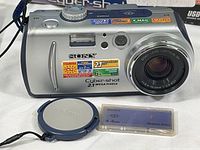 Front view of Sony Cyber-shot DSC-P50 digital camera showing detailed model and feature stickers, lens, shutter button, and flash with lens cap and 4MB memory stick case alongside.