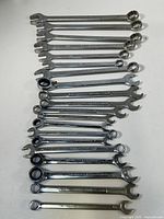 Photo showing an array of 17 combination wrenches laid out on a flat surface, sizes range from 3/8 inch to 1 inch, chrome finish, some rust spots visible.