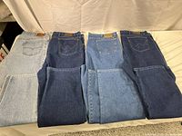 Four pairs of blue denim jeans from Wrangler and Levi's. Different shades of blue with visible stitching, folded and laid flat.
