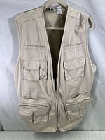 Front view of beige sleeveless fishing/hunting vest with multiple pockets and front zipper.