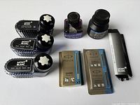 Top view of three Mont Blanc black ink bottles, purple Inkognito ink, black ink bottle, Parker Quink cartridge packs, Mont Blanc piston converter box.