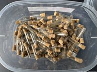 Clear plastic bin filled with many small glass tubes sealed with corks containing watch hands.