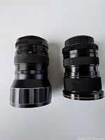 Side view of two vintage camera lenses side by side, showing physical design, focus and aperture rings.