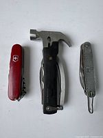 Top view of the red Swiss Army knife, vintage Camillus multi-tool hammer, and silver Swiss Army knife.