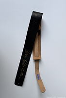 Full view of black leather guitar strap showing signatures and beige adjustable end.
