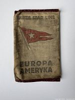 Front of vintage ticket holder showing White Star Line flag emblem and printed text 'Europa Ameryka'. Fabric shows signs of wear and discoloration.