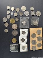 Full array of vintage coins including various international and commemorative coins with some coins in protective holders and envelopes.