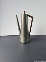 Front view of vintage pewter coffee pot with teak handle and knob on lid against plain background.
