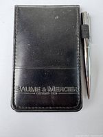 Front view of black leather Baume & Mercier notepad holder with attached chrome pen.