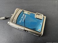 Olympus Stylus Tough 8000 digital camera shown from front angle on black surface. The blue front panel with 'Stylus Tough 8000' branding, 12MP mark, built-in flash, and lens cover are visible.