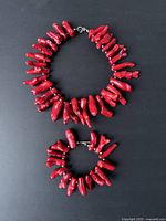 Full view of red coral necklace and bracelet set laid on a black background, showing the general shape and size of each item.