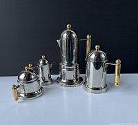 Full set of four vintage VEV Vigano coffee makers with stainless steel body and brass handles and knobs against black background.