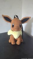 Front view of the Eevee knapsack on a flat surface, showing details of the face, ears, collar, and plush texture.