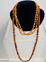 Three amber necklaces displayed on a black bust and stand, showing the length and bead shapes.