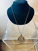 Full view of pendant hanging on necklace chain from front on display stand. Shows overall size and shape.