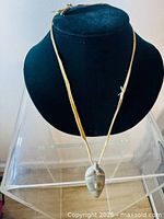 Full view of stone carved face pendant necklace on black display bust.