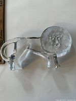 Front view of clear glass XL lion sculpture with textured mane and smooth body, ruler shown for scale.