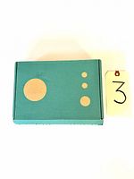 Closed turquoise box with three sized circular print patterns, numbered tag '3' alongside.