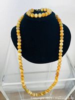 Full view of necklace and bracelet displayed on black bust stand, showing matching round stone beads in yellow-orange colors.