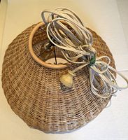 Top view of woven wicker lamp shade with bundled white electrical cord and pull chain with wooden pull piece.