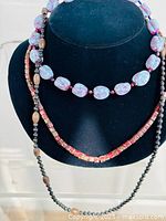 Three handmade mixed glass and stone bead necklaces displayed on a black bust stand.