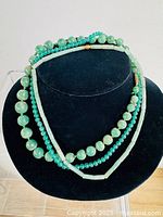 Three green necklaces displayed on black bust to show color and design composition