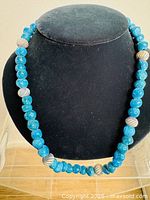 Front view of the full necklace displayed on a black velvet bust form, showing a continuous pattern of blue round beads with spaced accent beads.