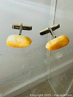 Front view of the pair of rectangular natural stone cufflinks with polished yellow-orange stone inlays and metal closure stamped PAT 2920363.