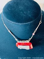 Photo of the full necklace displayed on a black velvet bust, showing the silver chain with bar and ring links and the signed pendant with red and silver design.