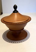 Front view of turned cherry wood bowl with lid and black finial handle on top