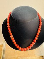 Full view of vintage coral beaded necklace on black display bust, showing full length and bead arrangement.