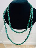 Two long green gemstone chip beaded necklaces displayed on a black bust, showing their length and bead style.