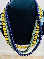Photo showing four vintage costume jewelry necklaces with mixed glass beads and natural stones on a black velvet display stand.