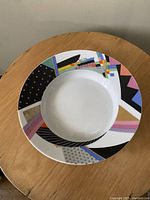 Top view of the Rosenthal serving bowl showing the colorful abstract geometric patterned rim around a white center on a wooden table.