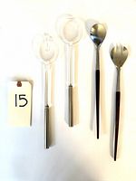 Four vintage serving utensils on white background, two Guzini with clear lucite handles, two likely Japanese with wood handles and stainless steel.