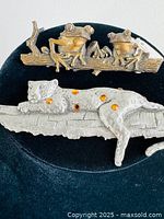 Both frog and jaguar brooches displayed on a black velvet background showing scale and details of each piece, highlighting their textures and finishes.