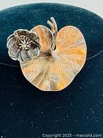 Front view of brooch showing heart-shaped leaf with raised flower detail and patina.