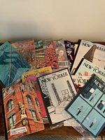 Collection of 12 New Yorker magazine issues spread out showing diverse illustrated covers including buildings, abstract art, and people.