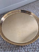 Photo of round gold plated serving tray with intricate engraved design on base and decorative pierced rim.