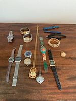All watches and rings displayed on a wooden surface including wristwatches, bracelet watches, ring watches, and pendant watch necklaces. Also includes a few replacement leather watch bands.
