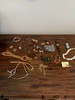 Photo of assorted costume jewelry laid out on wooden surface showing necklaces, bracelets, rings, earrings, and pins.
